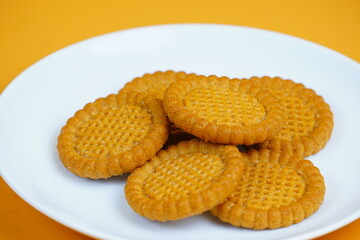 A plate of golden-brown, round, crunchy biscuits with a textured surface, set against an orange background.