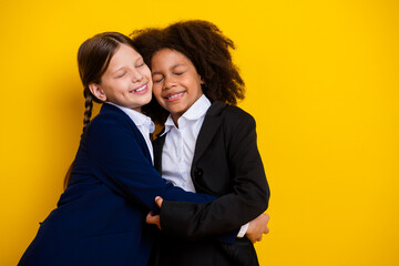 Two cheerful schoolgirls hugging joyfully against a vibrant yellow background, symbolizing friendship and togetherness