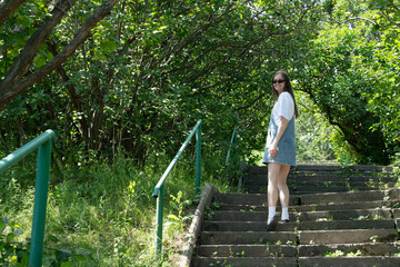 A young woman in casual attire climbs stone stairs amid lush greenery. Sunlight filters through trees, creating a vibrant atmosphere in the park