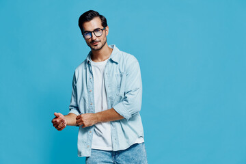 Stylish handsome young man with glasses posing confidently in light denim attire against a vibrant...