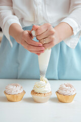 Close up hands of the chef with confectionery bag squeezing cream on cupcakes