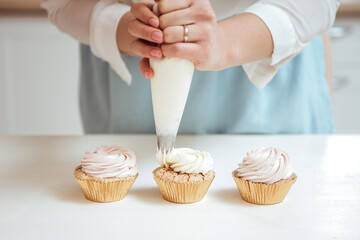 Close up hands of the chef with confectionery bag squeezing cream on cupcakes