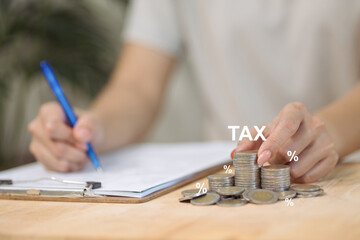 A person calculates taxes, with the word TAX and percentage symbols floating over stacks of coins.