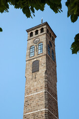 Historic Clock Tower Against a Clear Blue Sky Framed by Green Leaves.Sarajevo Uhrturm(Clock Tower)