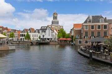 Panoramic canal view in Leiden, featuring the majestic Hartebrugkerk church and vibrant waterfront cafes. Perfect for showcasing European charm, historic architecture, and leisurely city life.