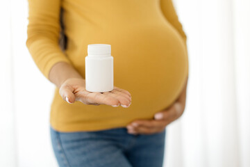 Closeup of pregnant woman holding supplement bottle in hand and touching belly. Symbol of prenatal...