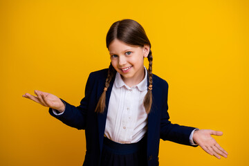 Confident schoolgirl in uniform smiling and gesturing against yellow background embracing learning and curiosity