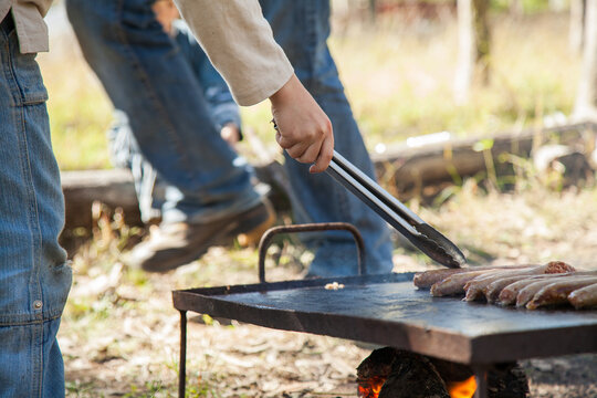 Boy cooking sausages on a bbq hot plate over a campfire