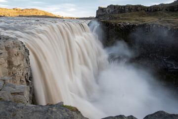 Dettifoss, Europe's most powerful waterfall, showcasing its immense force as milky glacial water plunges into a rocky canyon in Northeast Iceland under dramatic light