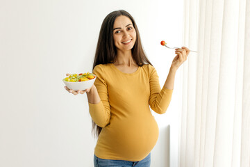 Smiling pregnant woman holding fresh salad and fork, promoting healthy nutrition, balanced prenatal...