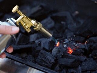 Person using a blowtorch to light charcoal in a grill