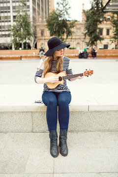 Young woman playing a ukulele on city street