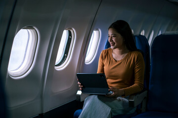 woman is sitting in an airplane seat with a laptop in front of her