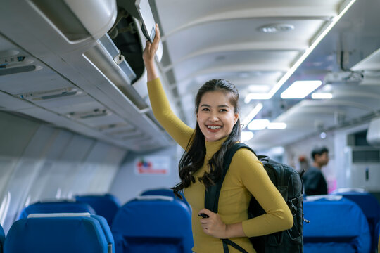 woman is smiling and holding a backpack while standing in an airplane