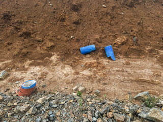 Blue drainage pipes and construction materials are scattered on dry, cracked earth, surrounded by...