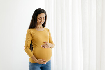 Pregnancy Concept. Portrait Of Smiling Young Pregnant Woman Embracing Belly While Standing Near...