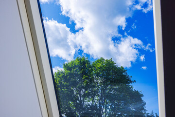 View through attic window showing green tree and white clouds against deep blue summer sky on sunny day. Sweden.