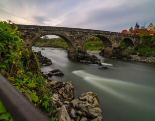 Fototapeta premium Ancient Stone Bridge Over a River in a Picturesque Landscape