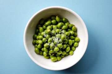 A white bowl filled with green peas on a blue surface.