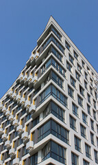Fototapeta premium Unusual architecture of an urban apartment building that resembles an iceberg with a curved corner section. Original design of residential building over blue sky background 