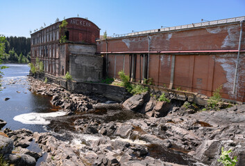 A brick hydroelectric power plant building of the early 19th century in Lyaskelya, Karelia, on the bank of a river with a forest