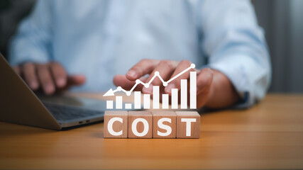 People working and wooden blocks spelling out the word COST, with a graph overlaying a downward trend, representing declining costs, cost analysis, financial management challenges, and economic trends
