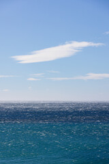 Strong gale force wind gusts blowing across a dark blue ocean's surface creating sea spray and small wave white caps.