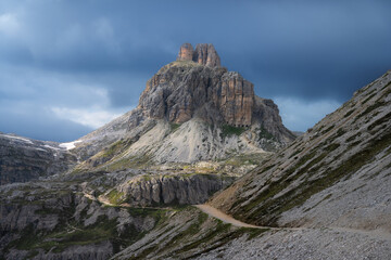 Tre Cime di Lavaredo mountains under dramatic cloudy sky, with a winding gravel path in summer. Dolomites, Italy. Landscape with rocks, trail, blue sky at sunset. Nature. Alpine mountains. Hiking