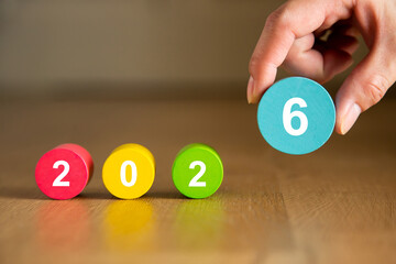 Hand placing the number six to complete the year 2026 with colorful wooden cylinders