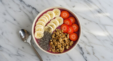 A vibrant smoothie bowl topped with sliced bananas, strawberries, granola, and chia seeds.