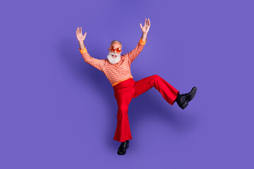 Charismatic senior man in vibrant retro attire dancing joyfully on a purple background, showcasing a trendy and stylish vintage look
