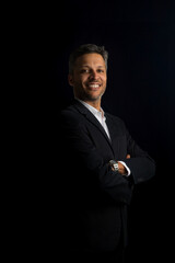 A man in a suit and tie is smiling and posing for a photo. He is wearing a watch and has his arms...