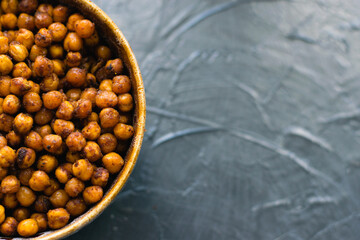 Delicious snack, fragrant baked with spices chickpeas in a brown bowl on a dark background with space for text. Healthy eating concept.