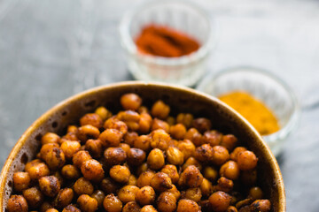 Delicious snack, fragrant baked with curry spices and smoked paprika chickpeas in a brown bowl and spices on a dark background with space for text. Healthy eating concept.