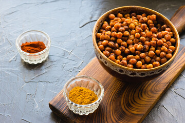 Delicious snack, fragrant baked with curry spices and smoked paprika chickpeas in a brown bowl and spices on a dark background with space for text. Healthy eating concept.