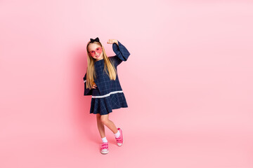 Smiling young girl in a stylish blue dress posing on a pink background with charm and confidence