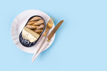Sardinecore trend concept, canned sardines in metal can on a blue background, on plate with a fork and knife