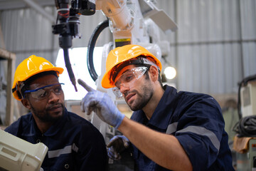 Blue collar workers at machine shop with welding robot arm.