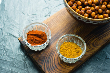 Delicious snack, fragrant baked with curry spices and smoked paprika chickpeas in a brown bowl and spices on a dark background with space for text. Healthy eating concept.