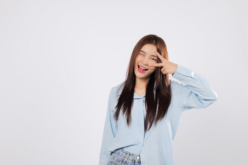 Victory sign near eye shows excitement, optimism, and joy. Victory moment of happy Asian woman captured against isolated a clean white background, expressing positive energy.
