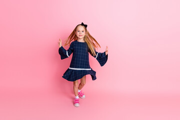 Charming young girl in casual dress posing against pink background, showcasing playful and vibrant...