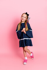 Charming young girl posing joyfully in a fashionable dress holding a wand, standing against a pink...