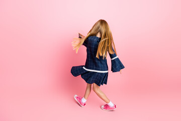 Young girl in stylish dress and sneakers spinning against pink background in joyful motion...