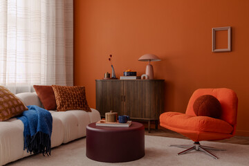 Stylish living room with a white sofa, orange accent chair, and layered throw pillows in rich textures. A vibrant orange wall serves as a bold and warm backdrop.