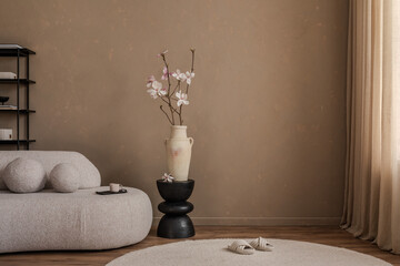Elegant interior with a sculptural pedestal and ceramic vase filled with pink magnolia branches, complemented by soft furniture and neutral decor.