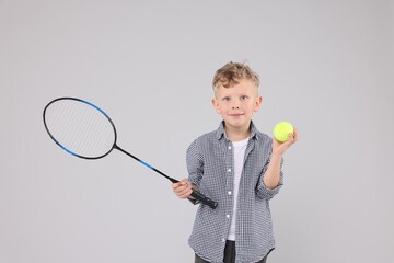 Little boy with racket and tennis ball on gray background