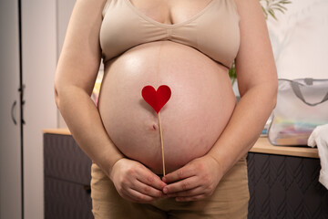Pregnant woman holding red heart shape and feel love for unborn baby in belly. Awaiting for baby. Concept of maternity and pregnancy care