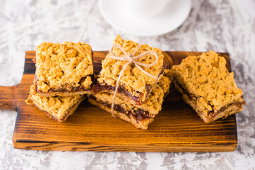 Delicious homemade pie with apple jam. Appetizing slices of grated pie with jam on a wooden board and coffee in a white cup on a light table.