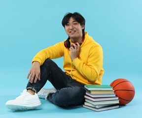 Student with books and basketball ball on light blue background