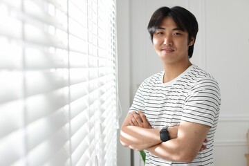 Portrait of handsome Asian man with crossed arms at home. Space for text